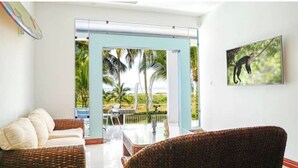 A room with a wicker sofa, a dining table, and a view of a garden and palm trees. - Oceanfront Pool Paradise Villa (Provincia de Puntarenas)