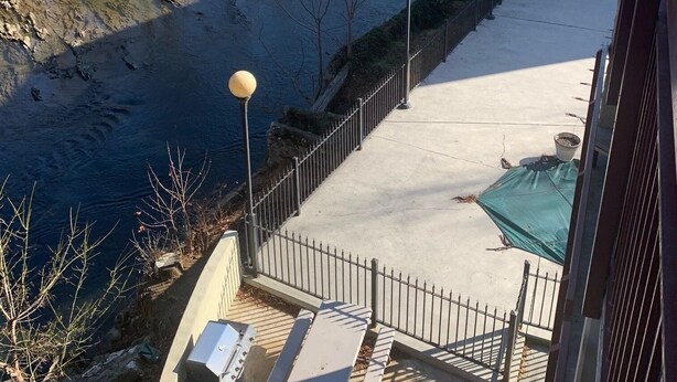 Eine Terrasse am Flussufer mit Betonboden, Metallgeländern und einem kleinen Tisch.