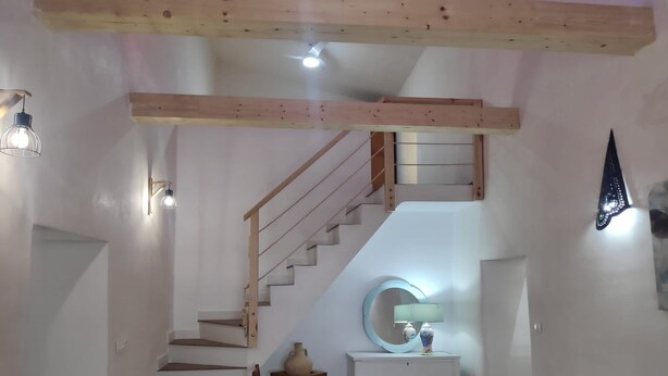 A staircase with wooden railings leading to an upper level, a round mirror on a white console table, and a dining area with a glass table and wooden chairs.