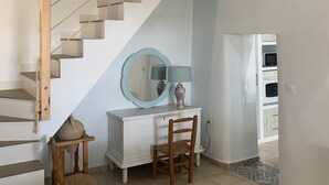 A staircase with wooden railings, a round mirror, a lamp, and a chair in a room with tiled flooring and a white dresser.