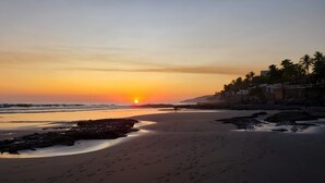 Una playa con atardecer, costa rocosa y palmeras.
