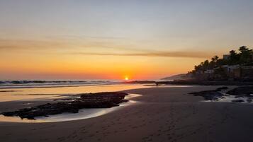 A beach with a sunset, rocky shoreline, and palm trees.