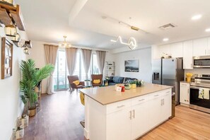 Une cuisine moderne avec des meubles blancs, un îlot central, des appareils en acier inoxydable et un coin repas comprenant un canapé et des chaises.