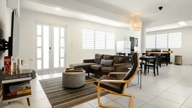 A spacious living room with a sofa, ottoman, and a dining area with chairs and a table. - Home in the heart of the city (Guaynabo)