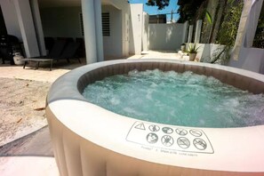 Un jacuzzi al aire libre con una etiqueta de advertencia de seguridad, rodeado de una zona de patio con sillas de descanso y plantas en macetas.