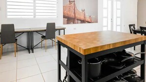 A modern kitchen with a wooden countertop and black metal shelving, a large window with blinds, and a painting of a bridge on the wall. - Home in the heart of the city (Guaynabo)