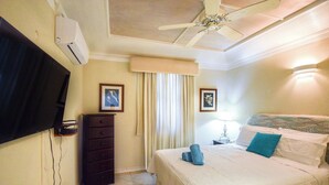 Habitación de hotel con cama, cómoda, televisor, ventilador de techo y ventana con cortinas.