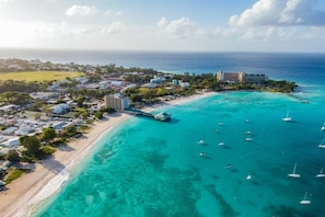 An aerial view of a coastal resort with a beach, clear turquoise waters, and several boats.