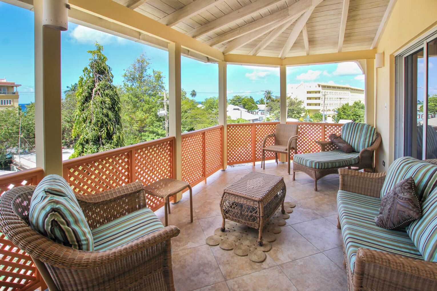 Un balcon abrité, doté de meubles en osier, offrant une vue sur la mer et situé dans un cadre tropical.