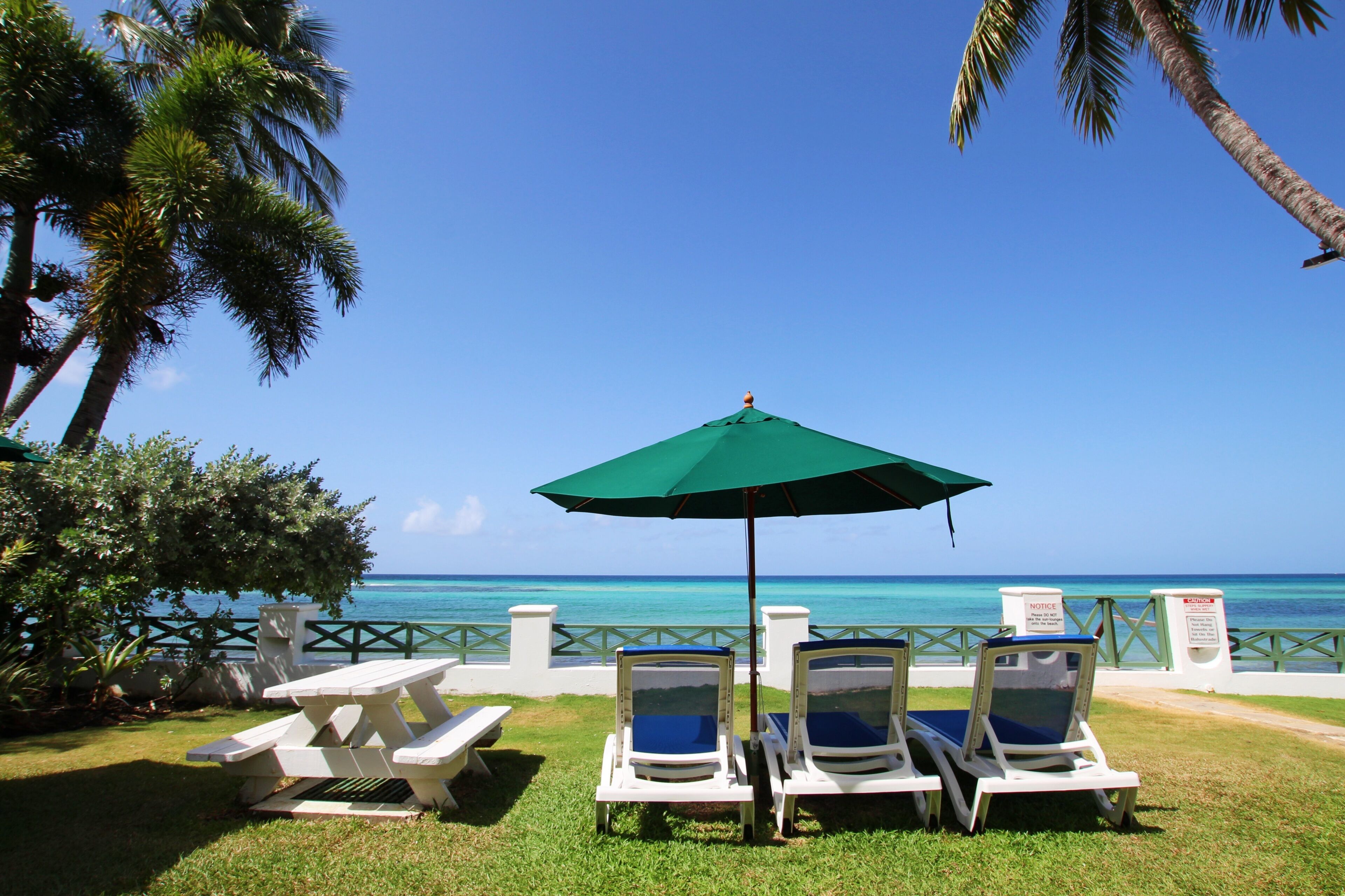 A beachside lounge with a table and chairs under a green umbrella, overlooking the ocean.