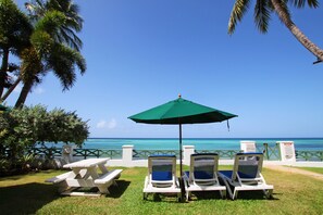 A beachside lounge with a table and chairs under a green umbrella, overlooking the ocean.
