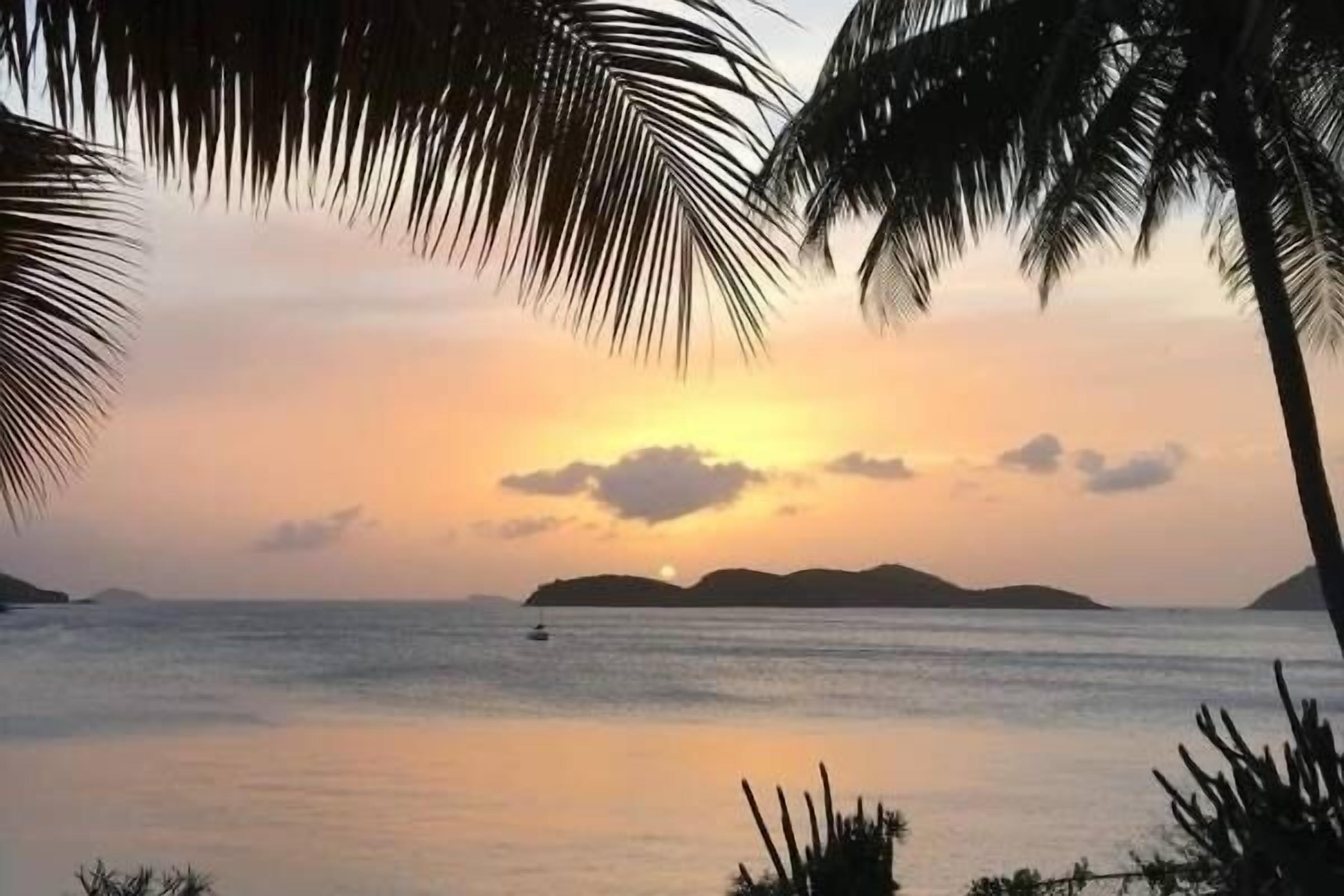 A sunset over calm waters with silhouettes of islands and palm trees framing the view.