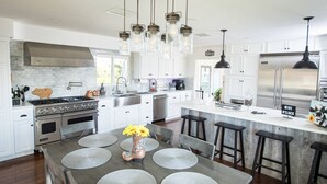 A modern kitchen with white cabinetry, a stainless steel stove, and a large island with bar stools. - Elevate Your Wine Country Escape: Chick-Ranch with Luxurious Amenities, Views, Private Driver (Temecula)