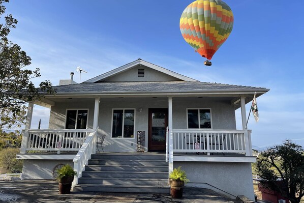 Een huis met twee verdiepingen, een veranda, een bord met 'Welkom' en een luchtballon aan de hemel.