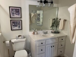 A bathroom with a toilet, sink, and mirror. There are framed pictures on the wall and a towel rack.