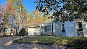 A single-story house with a covered porch, a stone retaining wall, and a well-maintained lawn. - GOLFERS GETAWAY (Hot Springs)