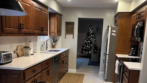 A modern kitchen with wooden cabinets, a dining table with chairs, a refrigerator, and a Christmas tree in the background. - GOLFERS GETAWAY (Hot Springs)