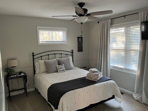 A bedroom with a bed, a ceiling fan, a window with blinds, a bedside table with a lamp, and a wall-mounted TV. - GOLFERS GETAWAY (Hot Springs)