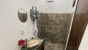 Un baño con ducha de piedra, tocador de madera con espejo y un inodoro.