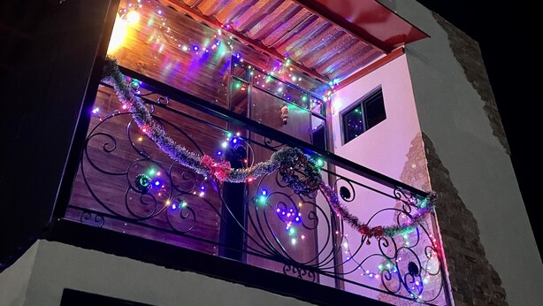 Un edificio con un balcón decorado con luces y guirnaldas de colores, un toldo rojo y una ventana con una reja metálica ornamental.