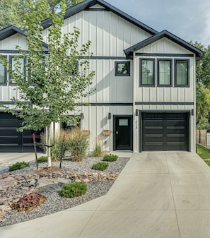 Une maison à deux étages avec un garage, une allée et un jardin aménagé avec des rochers et de petites plantes.