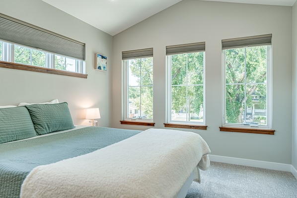 Une chambre avec un grand lit, trois fenêtres et une vue sur les arbres.