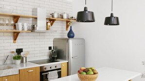 Una cocina con armarios de madera, encimera blanca, refrigerador y un bol de fruta en la encimera.