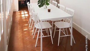 Un comedor con una mesa y sillas blancas, una planta en maceta y dos lámparas colgantes.
