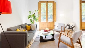 Una sala de estar con sofá, sillones, una mesa de centro y un ventanal con contraventanas de madera.