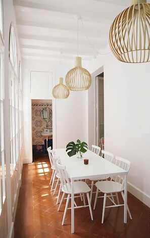 Un comedor con una mesa y sillas blancas, una planta en maceta y dos lámparas colgantes.