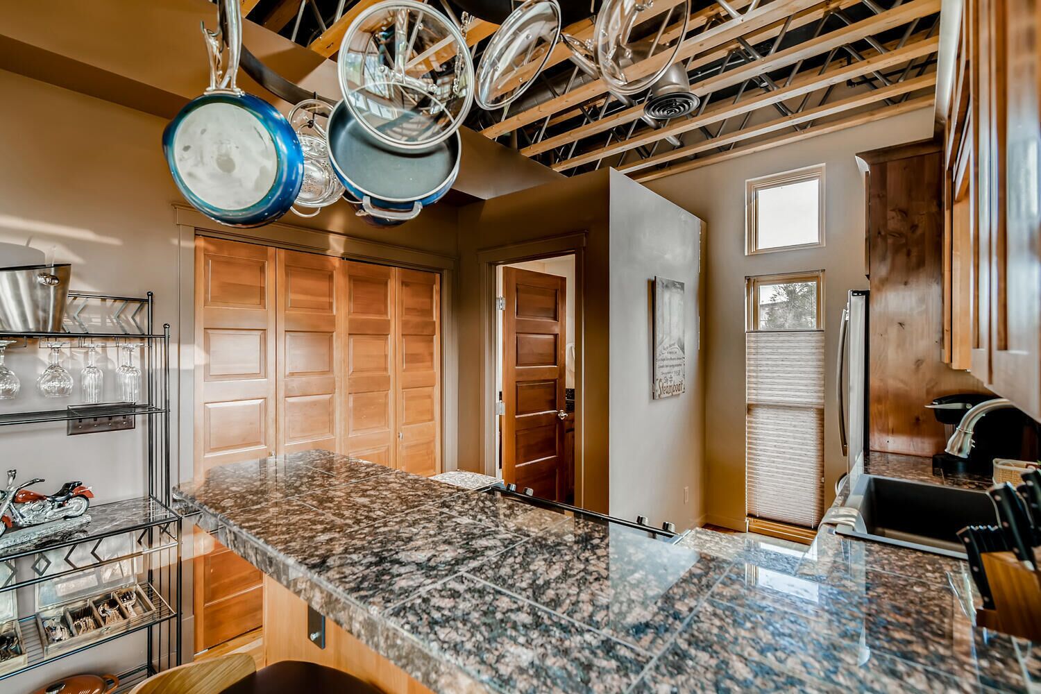 A kitchen with granite countertops, wooden cabinets, and a hanging pot rack.