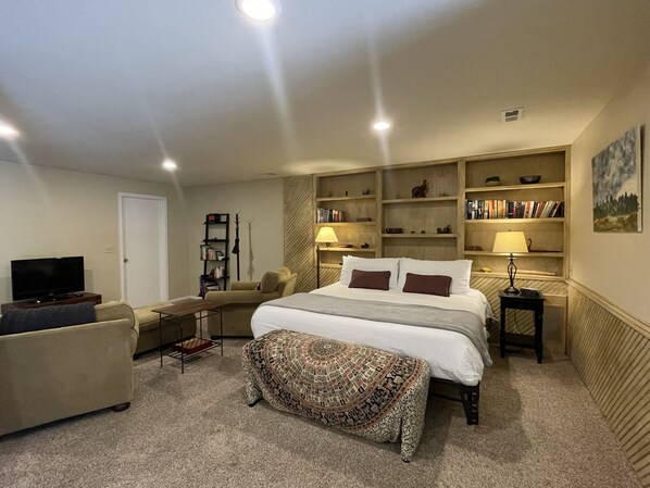 A bedroom with a large bed, a sofa, a television, a bookshelf, and a painting on the wall.