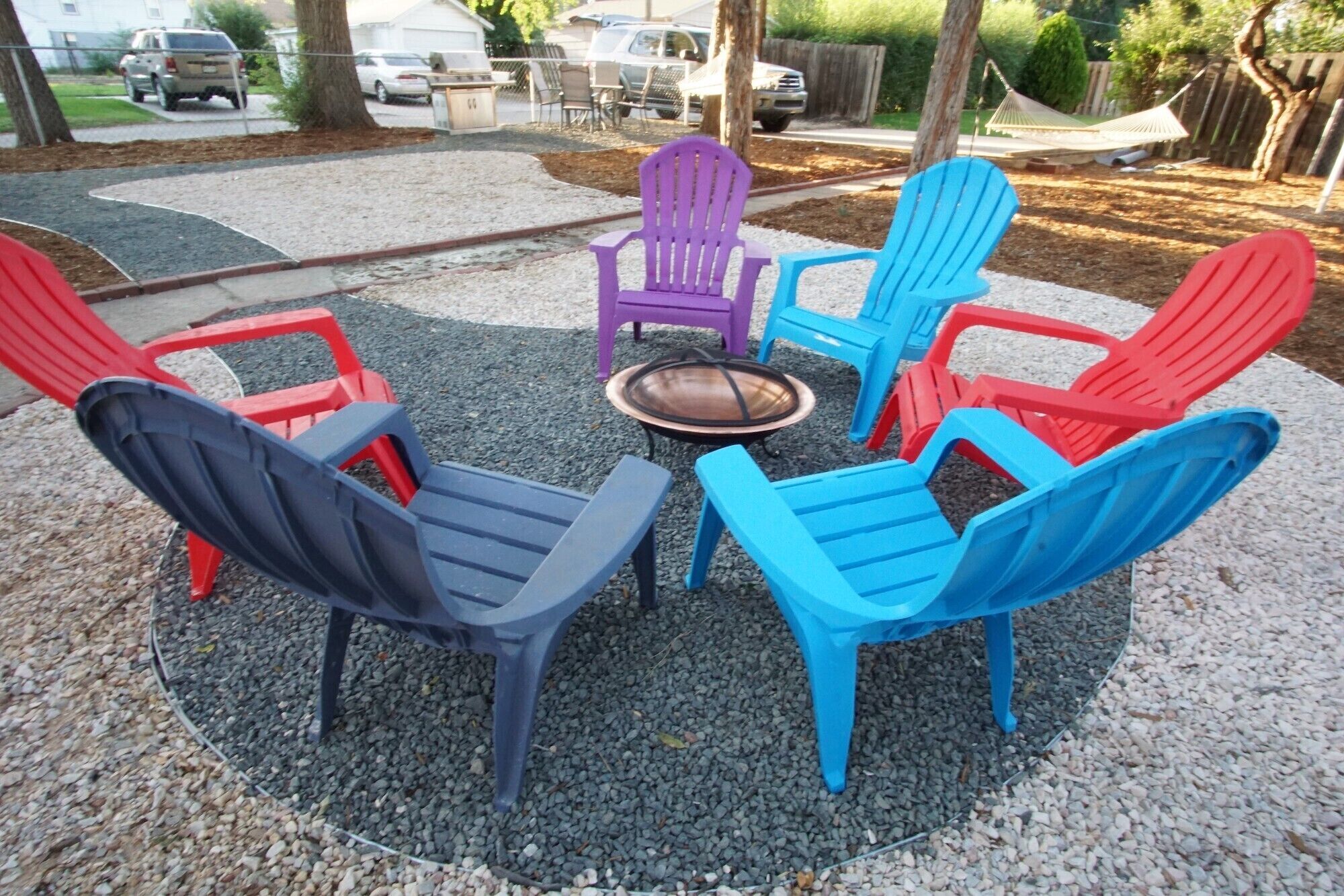 A circular outdoor seating area with colorful plastic chairs and a central fire pit.