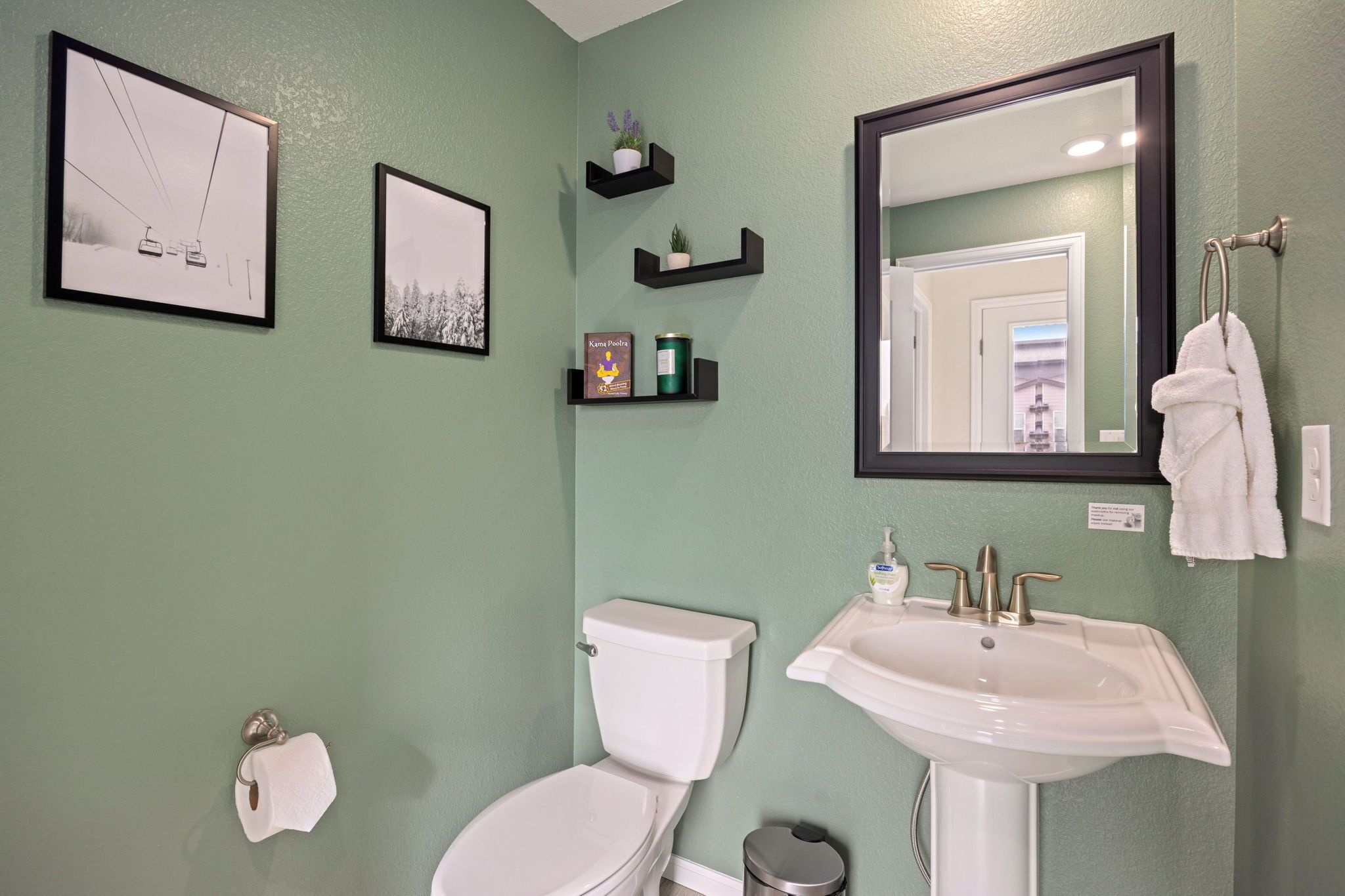 A bathroom with a toilet, sink, and framed pictures on the wall.