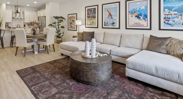 A modern living room with a grey sofa, a round coffee table, and a dining area with a white table and chairs.