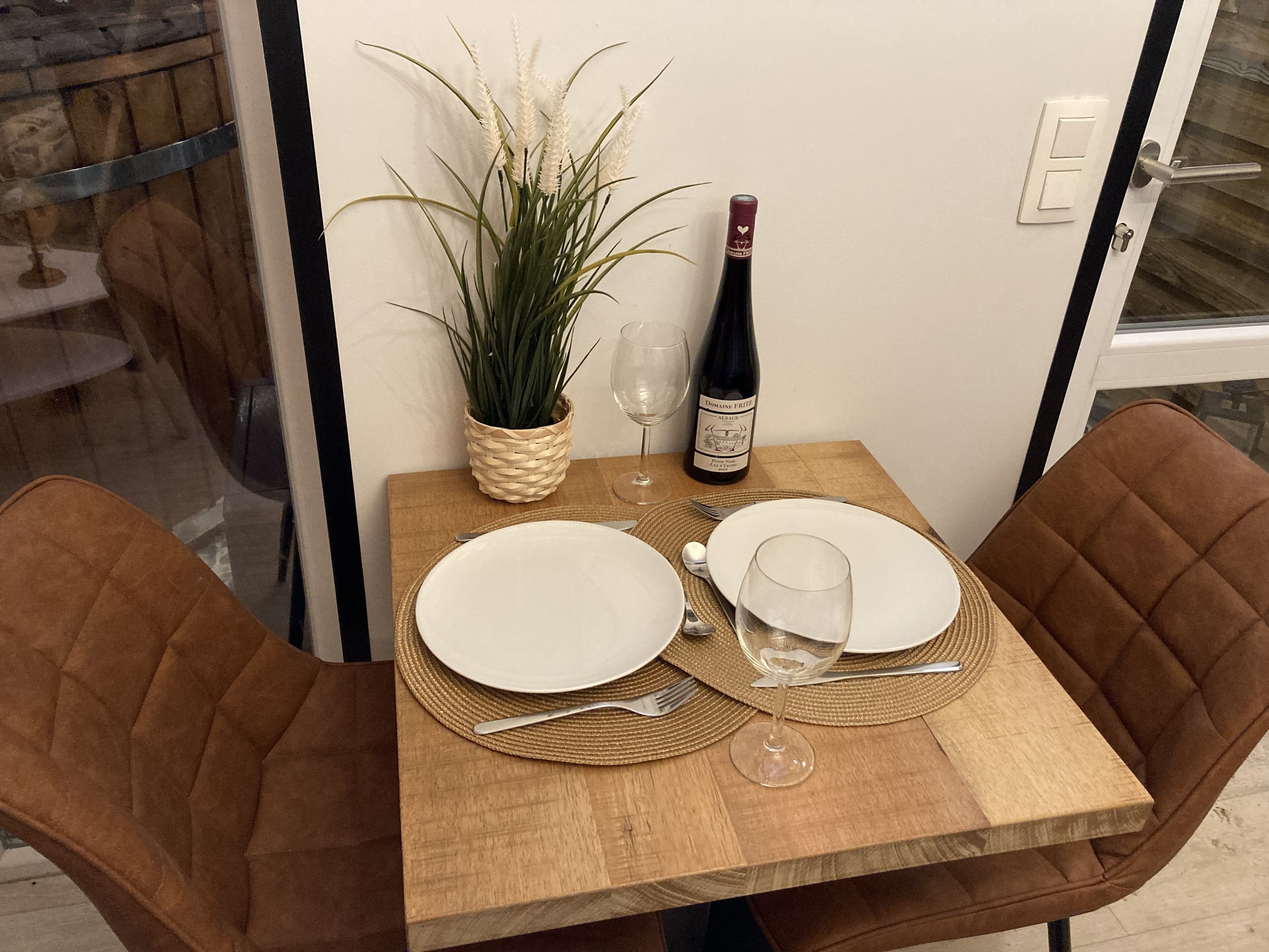 A dining table set with plates, cutlery, a wine bottle, and a glass.