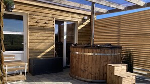En træhytte med jacuzzi, bænk og dør ind til indgangen.