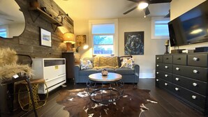 A cozy living room with a cowhide rug, a round coffee table, a sofa with decorative pillows, a fireplace, a TV, and a ceiling fan.