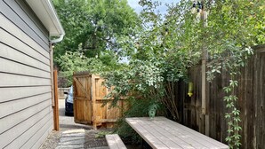 A patio with a picnic table, stone pathway, wooden fence, and a wooden structure in the background.