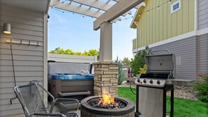Un patio al aire libre con un pozo de fuego de piedra, una parrilla y mobiliario de exterior.