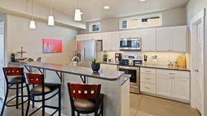 Una cocina moderna con armarios blancos, electrodomésticos de acero inoxidable y una isla central con taburetes de bar.