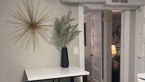 Uma pequena área de refeições com uma mesa branca e cadeiras pretas, um objeto decorativo na parede e um vaso com planta.