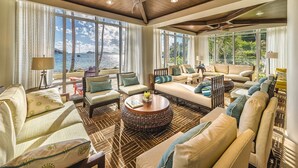 Un salón amplio con un gran ventanal con vistas al mar, amueblado con sofás, sillones y una mesa de centro redonda.