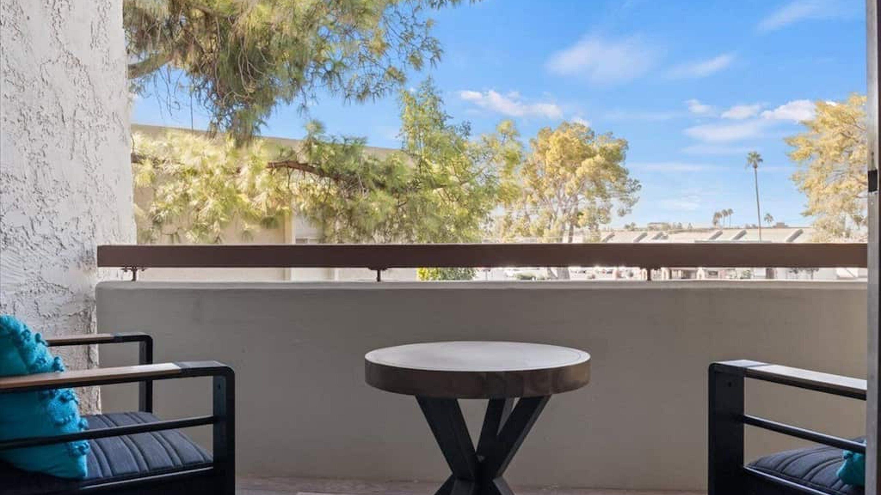 A balcony with a round table and two chairs, overlooking a clear sky and trees.