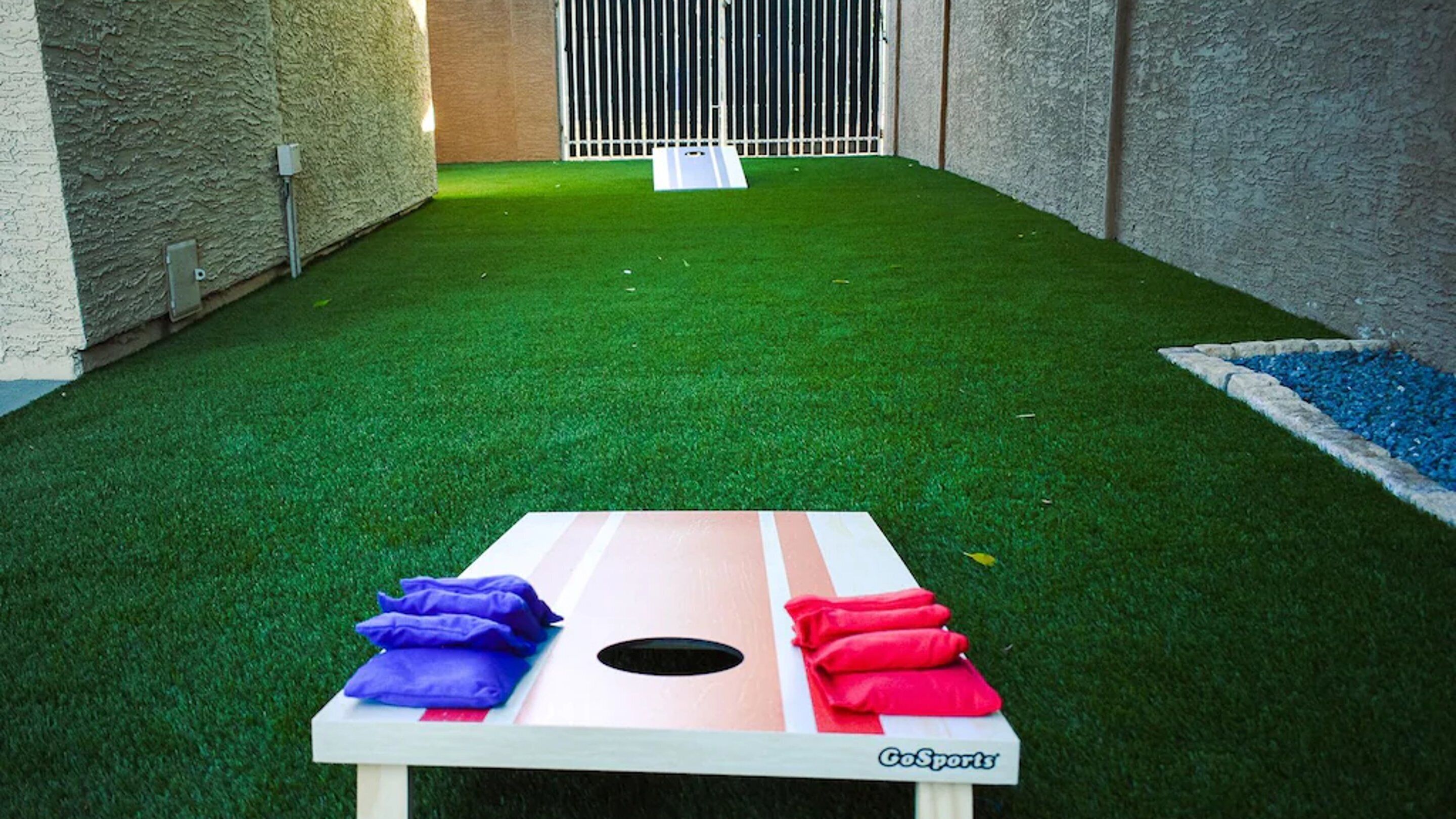 A CoSports game table with a hole in the middle, surrounded by artificial green turf and a white wall.
