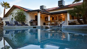 Un espace aménagé au bord de la piscine, avec des chaises longues, un barbecue et une terrasse décorée de guirlandes lumineuses.