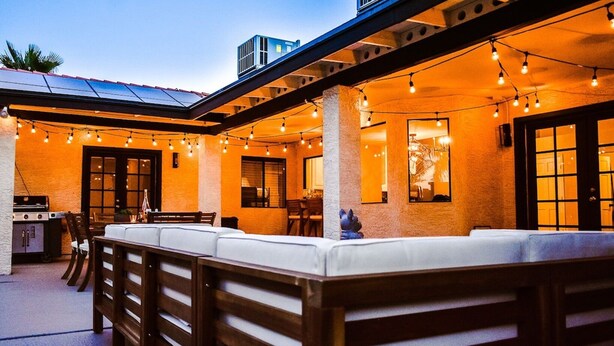 Un espace extérieur aménagé en terrasse, avec un long banc en bois, des guirlandes lumineuses et un barbecue.