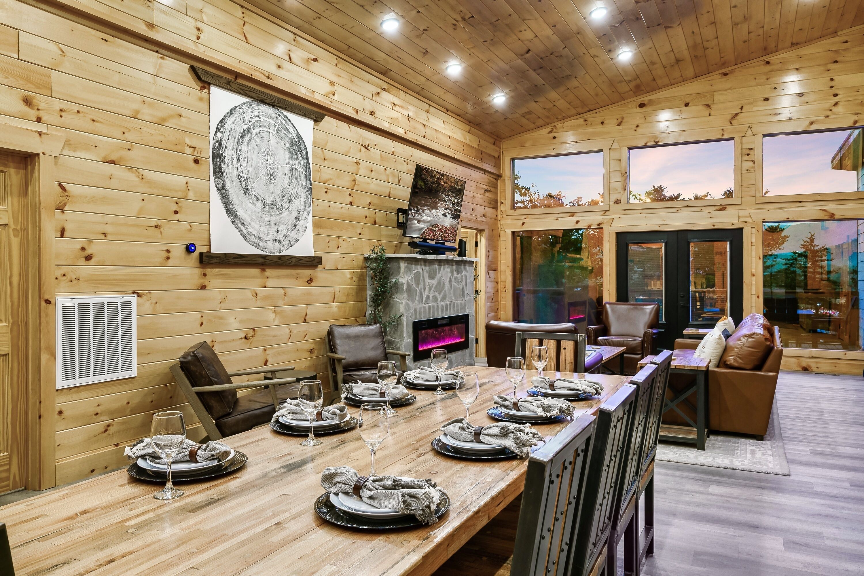 A wooden interior with a dining table set for six, a fireplace, and a seating area with leather chairs and sofas.