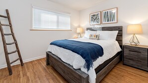 Ein Schlafzimmer mit einem hölzernen Bett, weißer Bettwäsche, einer blauen Tagesdecke, zwei Nachttischlampen und einem Nachttisch aus Holz.