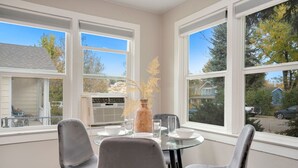 A dining area with a glass table, two grey chairs, and a vase with dried plants. - Charming Old Town Bungalow W/ Free Cruiser Bikes (Fort Collins)